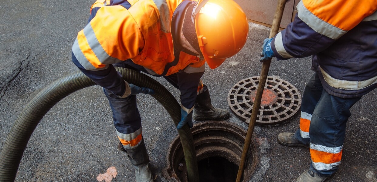 Worker cleaning a drain pipe with specialized equipment.