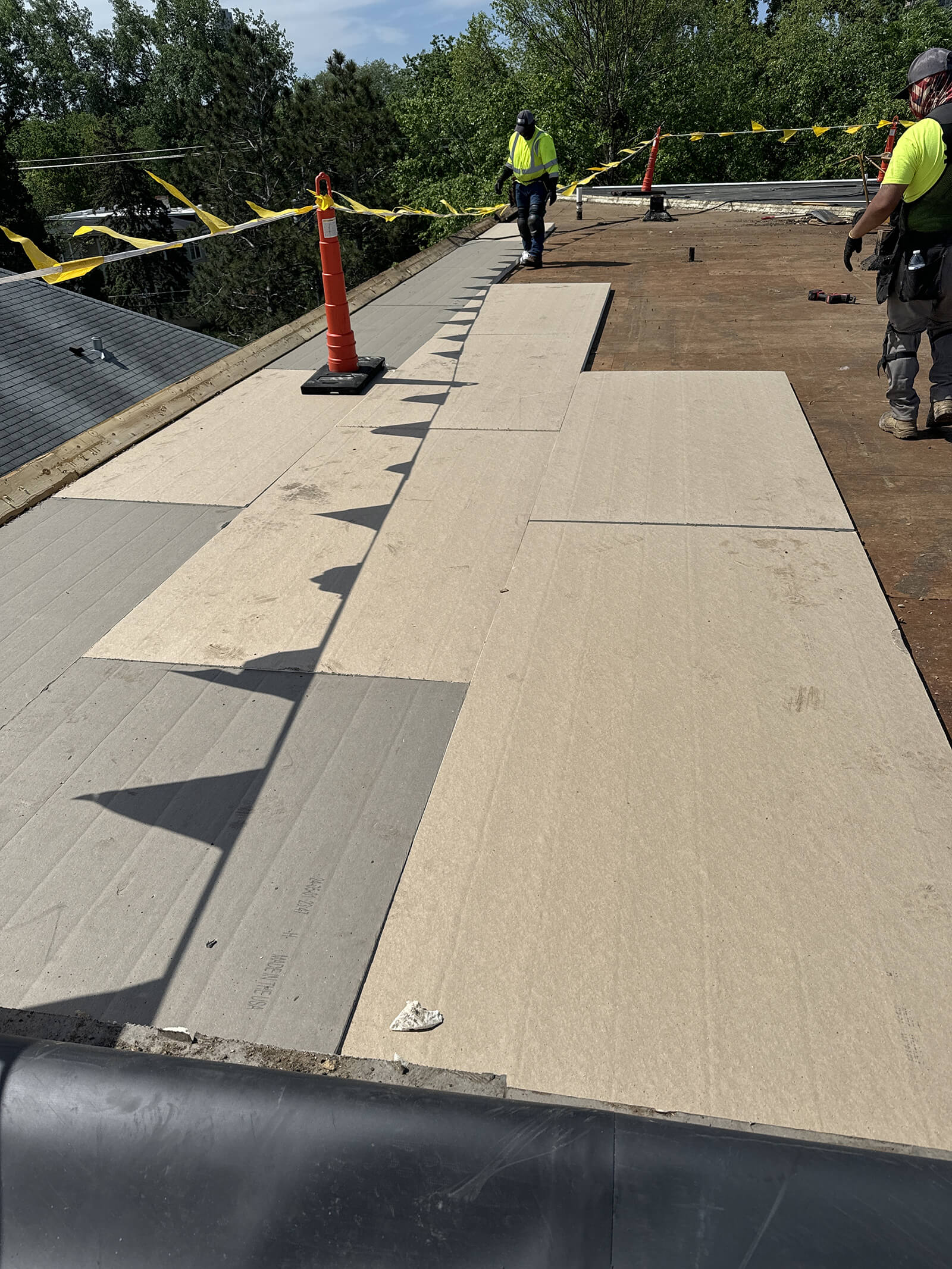 Construction workers installing insulation panels on a flat roof during a roof renovation project, with safety cones and caution tape marking the area.