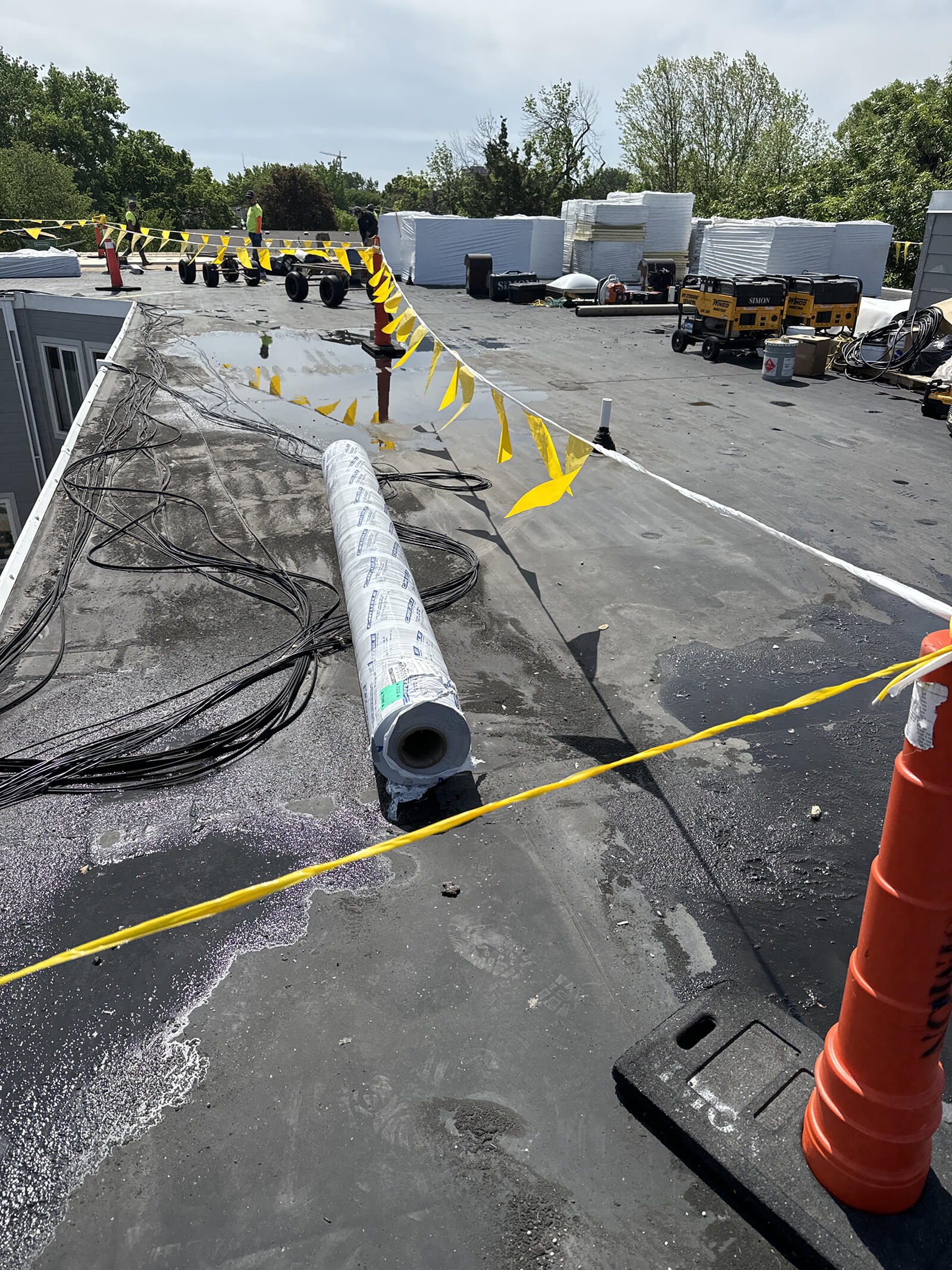 A flat roof undergoing renovation, with equipment, supplies, and construction workers preparing the area for new roofing materials.