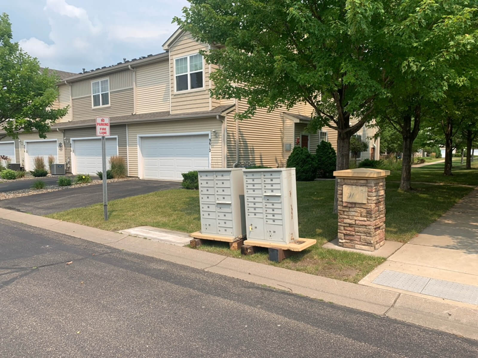 A suburban townhome community with a row of houses and mailboxes located on the sidewalk, next to a "No Parking Fire Lane" sign.