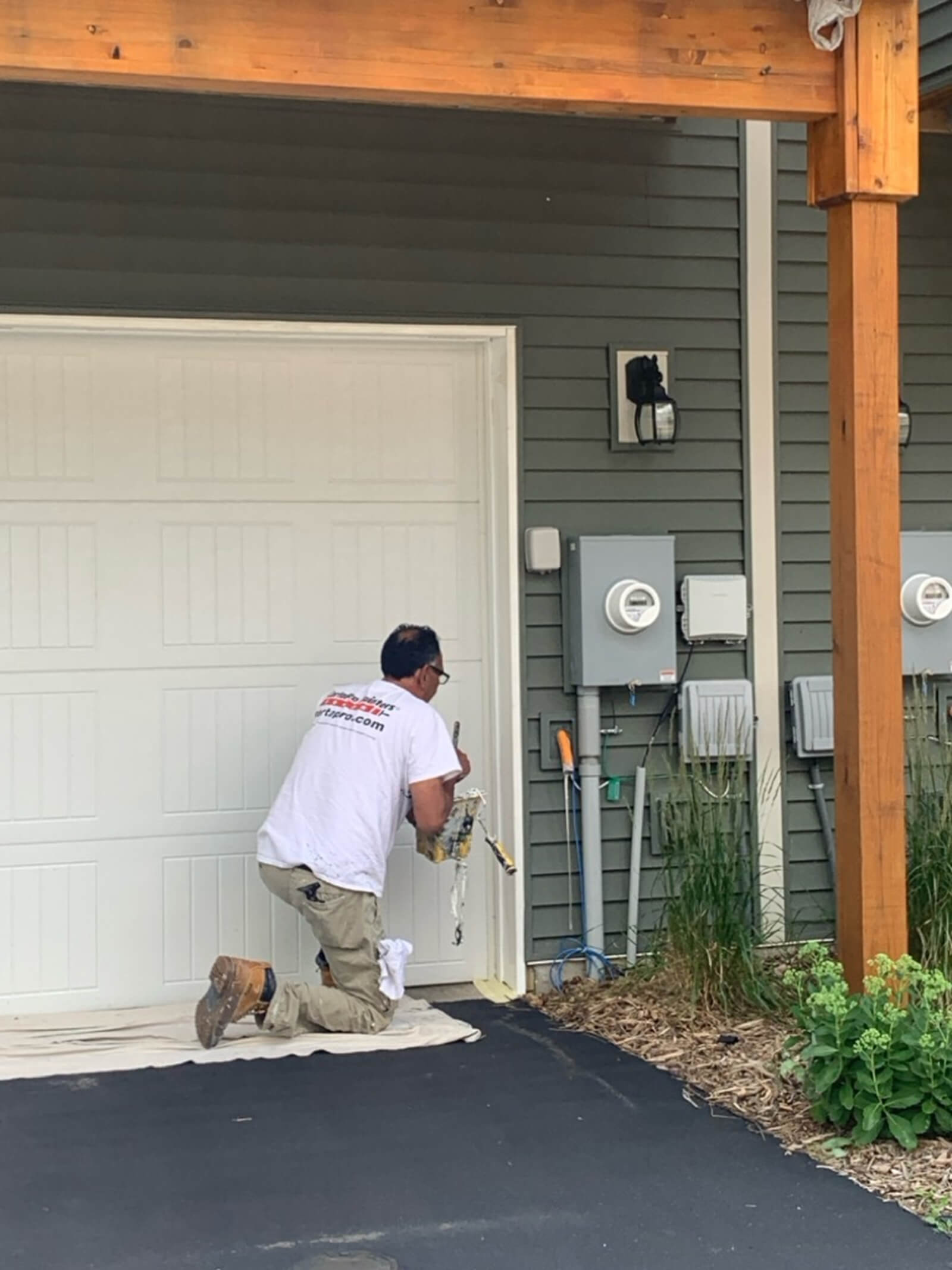 A construction worker applying caulk around the garage door trim of a residential home during a maintenance or renovation project.