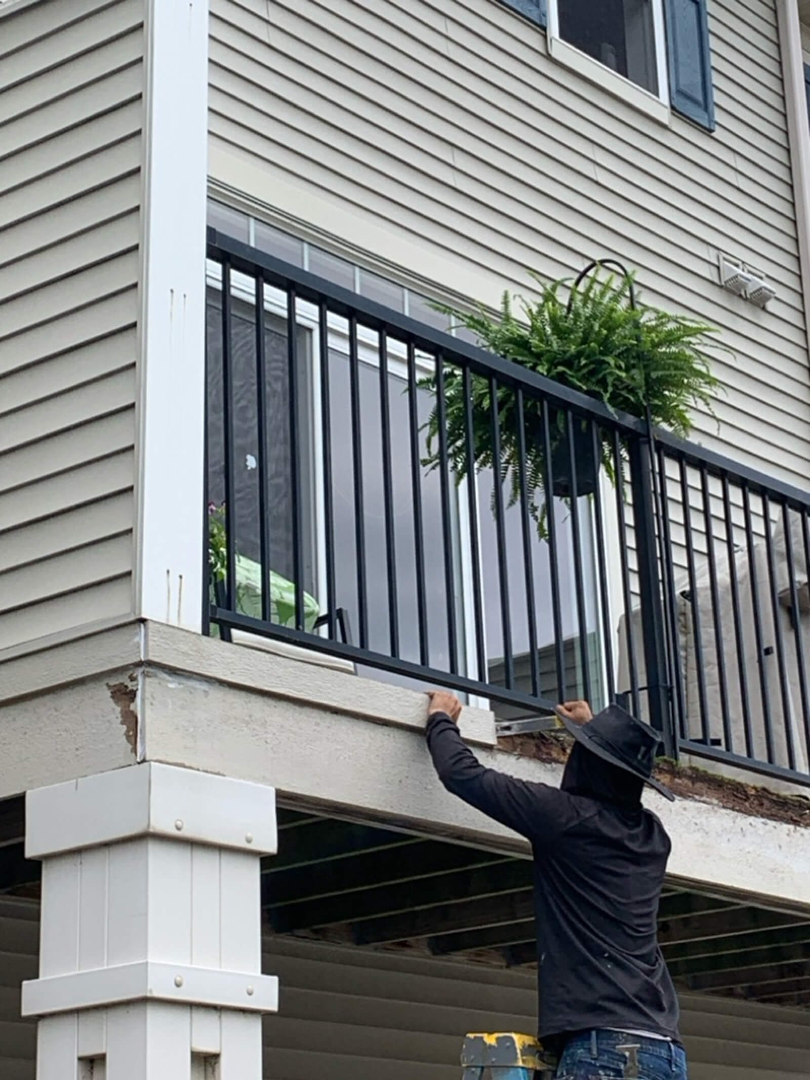 A construction worker making repairs to a balcony support structure on a residential home, carefully measuring and adjusting materials.