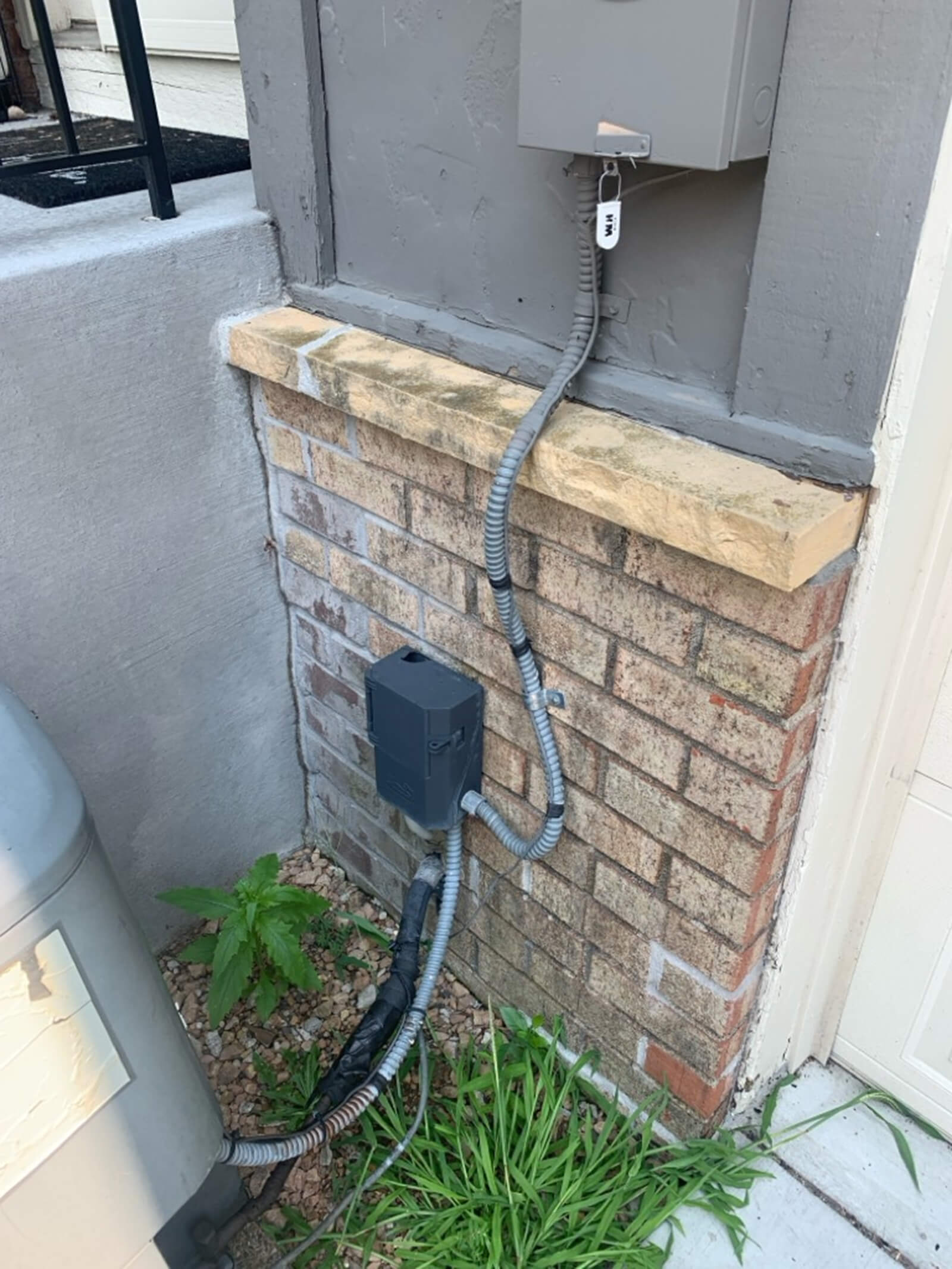 Close-up of a newly installed electrical box and conduit on the exterior of a residential home, neatly attached to a brick wall.