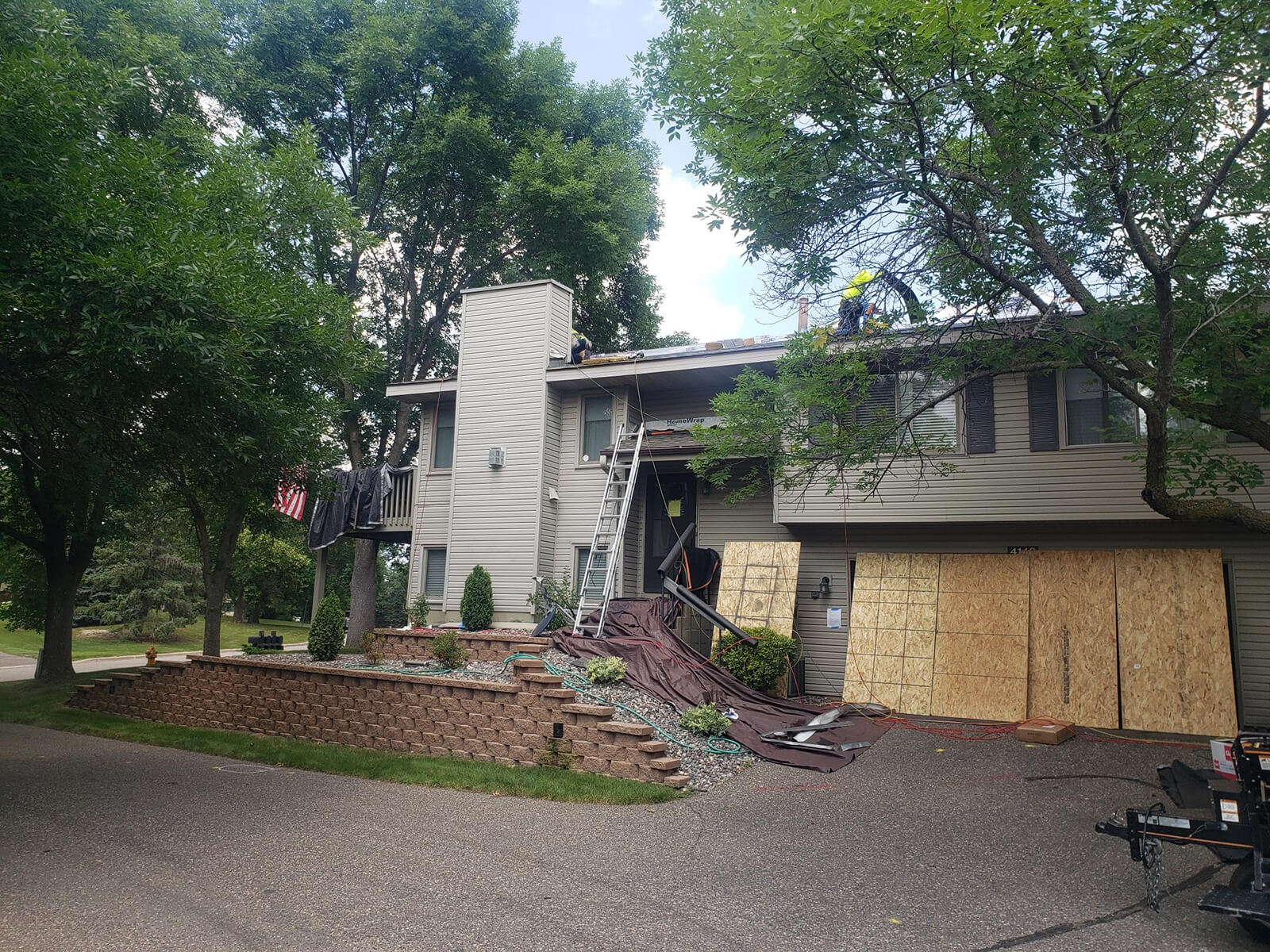 residential house with its roof under renovation, scaffolding, and boarded-up windows with workers seen on the roof.