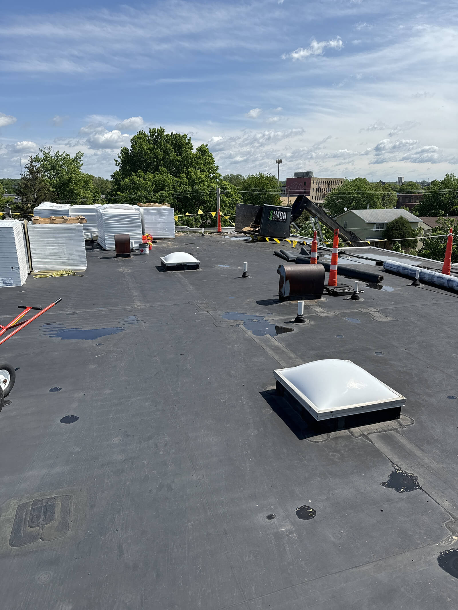 A flat commercial building roof with stacked roofing materials, skylights, and safety cones set up for roof renovation.