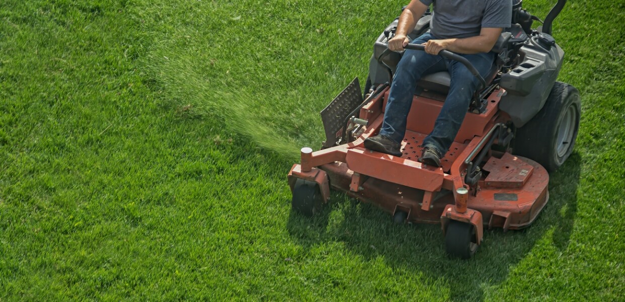 Worker mowing a lush green lawn with a riding lawn mower.