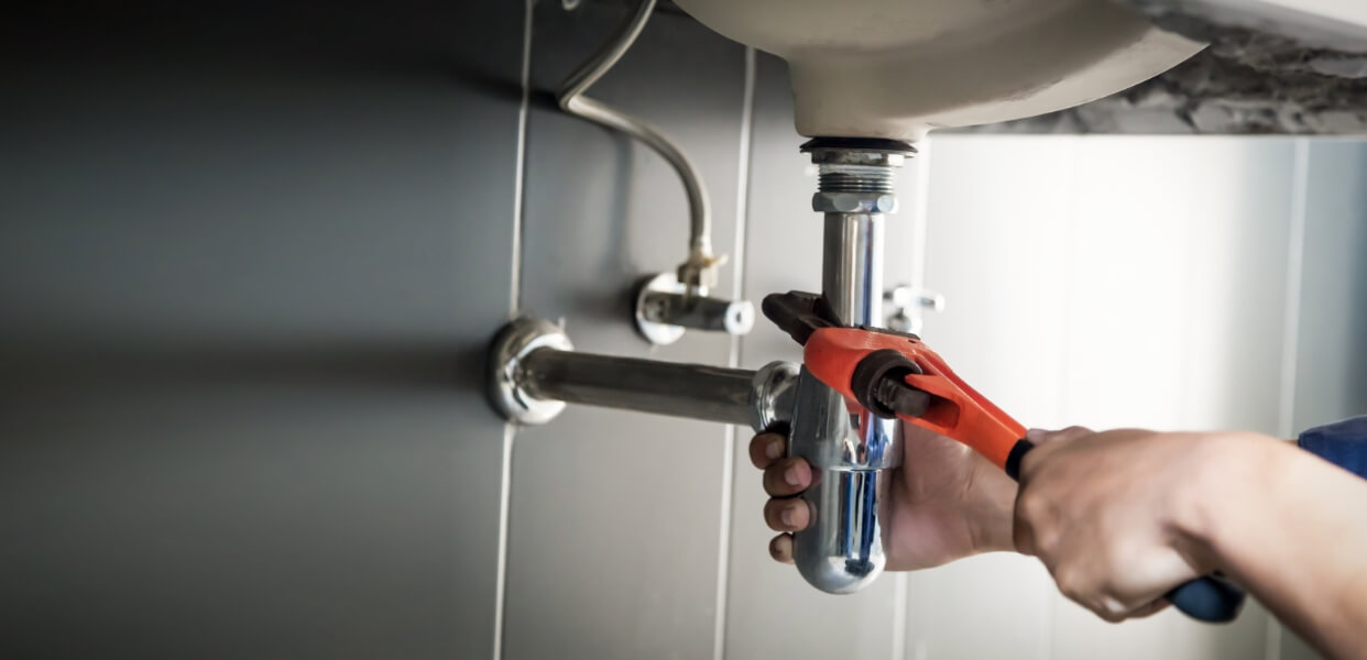 Plumber using a wrench to fix a pipe under a sink.