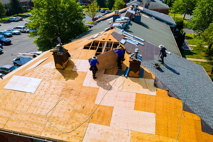 Construction workers repairing the roof with wooden panels on a residential building.