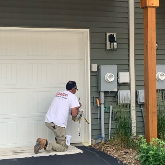 A construction worker applying caulk around the garage door trim of a residential home during a maintenance or renovation project.